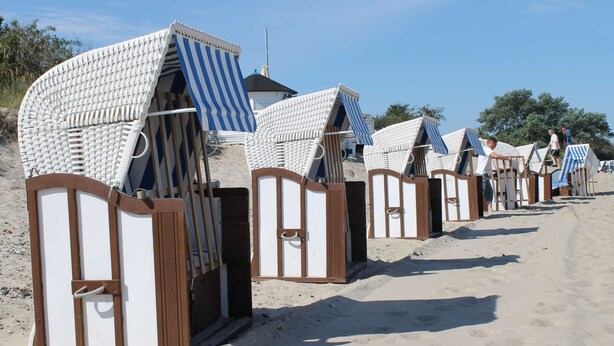 Strandhuse med stribede markiser, trærammer og en sandstrand i baggrunden.