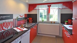 A modern kitchen with red and white cabinetry, a black countertop, and a window with a red curtain. - Komfort und Naturflucht, Lichtenhain (Sebnitz)