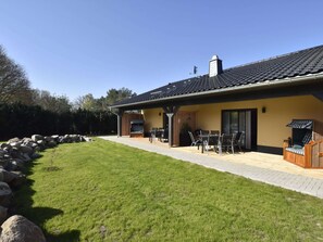A house with a patio area, outdoor seating, and a stone wall. - Schones Ferienhaus in Barnekow mit Kamin (Barnekow)