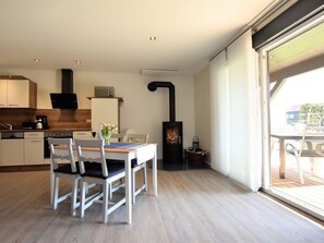 A modern kitchen with white cabinets, a dining table with chairs, a built-in microwave, and a wood-burning stove. - Schones Ferienhaus in Barnekow mit Kamin (Barnekow)