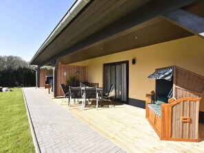 A covered patio area with a dining table and chairs, a wicker sofa, and a grill. - Schones Ferienhaus in Barnekow mit Kamin (Barnekow)