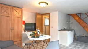 Un espace de vie compact comprenant une table à manger, deux chaises, un canapé, un téléviseur et un coin cuisine.