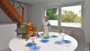 Une table à manger avec une bouteille de vin, deux verres et un centre de table composé de fleurs.