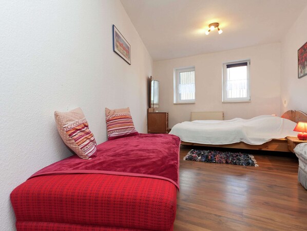 Een slaapkamer met twee bedden, een houten vloer en een plafondlamp.