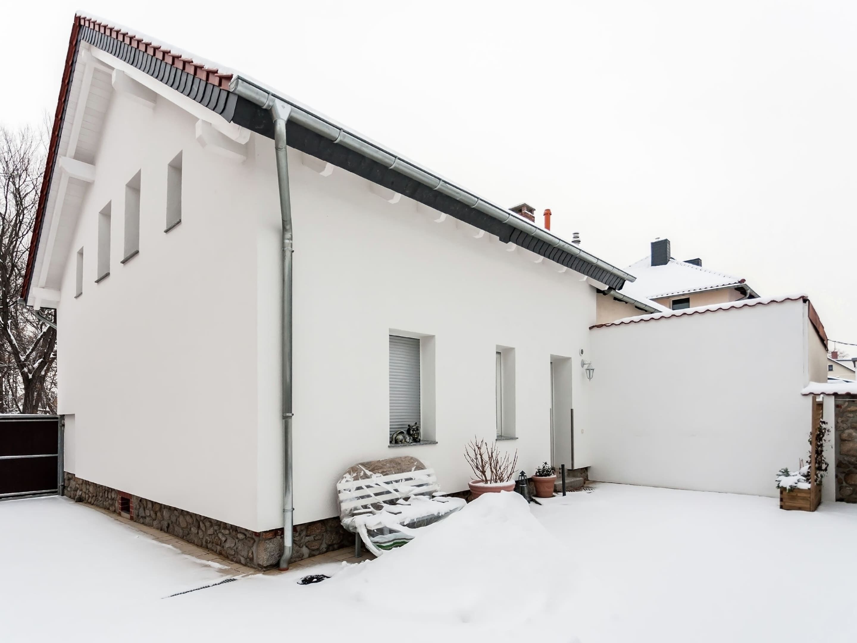 Un edificio blanco con techo inclinado, una chimenea y una estructura pequeña adosada.