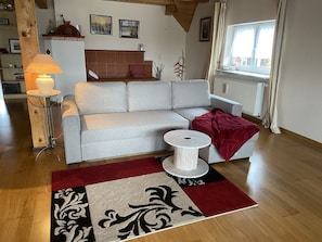 A living room with a sofa, a lamp, a small table, a red throw blanket, and a patterned rug.