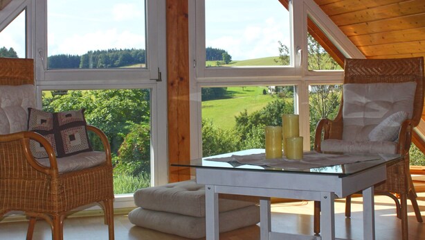 A room with wicker chairs, a glass-top table, and large windows offering a view of a green landscape. - Alpine Stay in Herrischried (Herrischried)