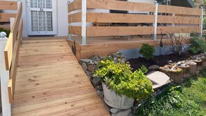 A wooden deck leading to a house with a white exterior, a heart-shaped decoration on the door, and a small window with a plant. - Alpine Stay in Herrischried (Herrischried)