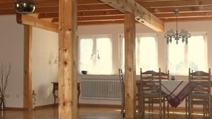 A spacious room with wooden beams, a dining table with chairs, a chandelier, and a large window. - Alpine Stay in Herrischried (Herrischried)