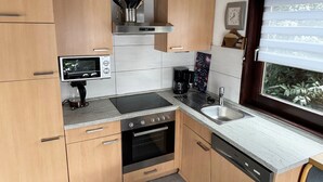 Eine moderne Küche mit Holzschränken, einem eingebauten Backofen, einem Geschirrspüler und einem Fenster mit Jalousien.