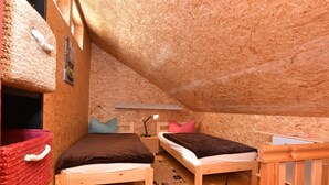 Une chambre mansardée chaleureuse avec deux lits en bois, un panier rouge et un bureau.