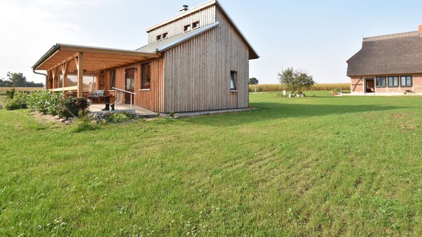 Une maison moderne en bois, dotée d’un porche abrité et d’une grande pelouse ouverte.