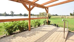 Une terrasse en bois offrant une vue sur un lac, entourée de verdure et d’un champ herbeux.