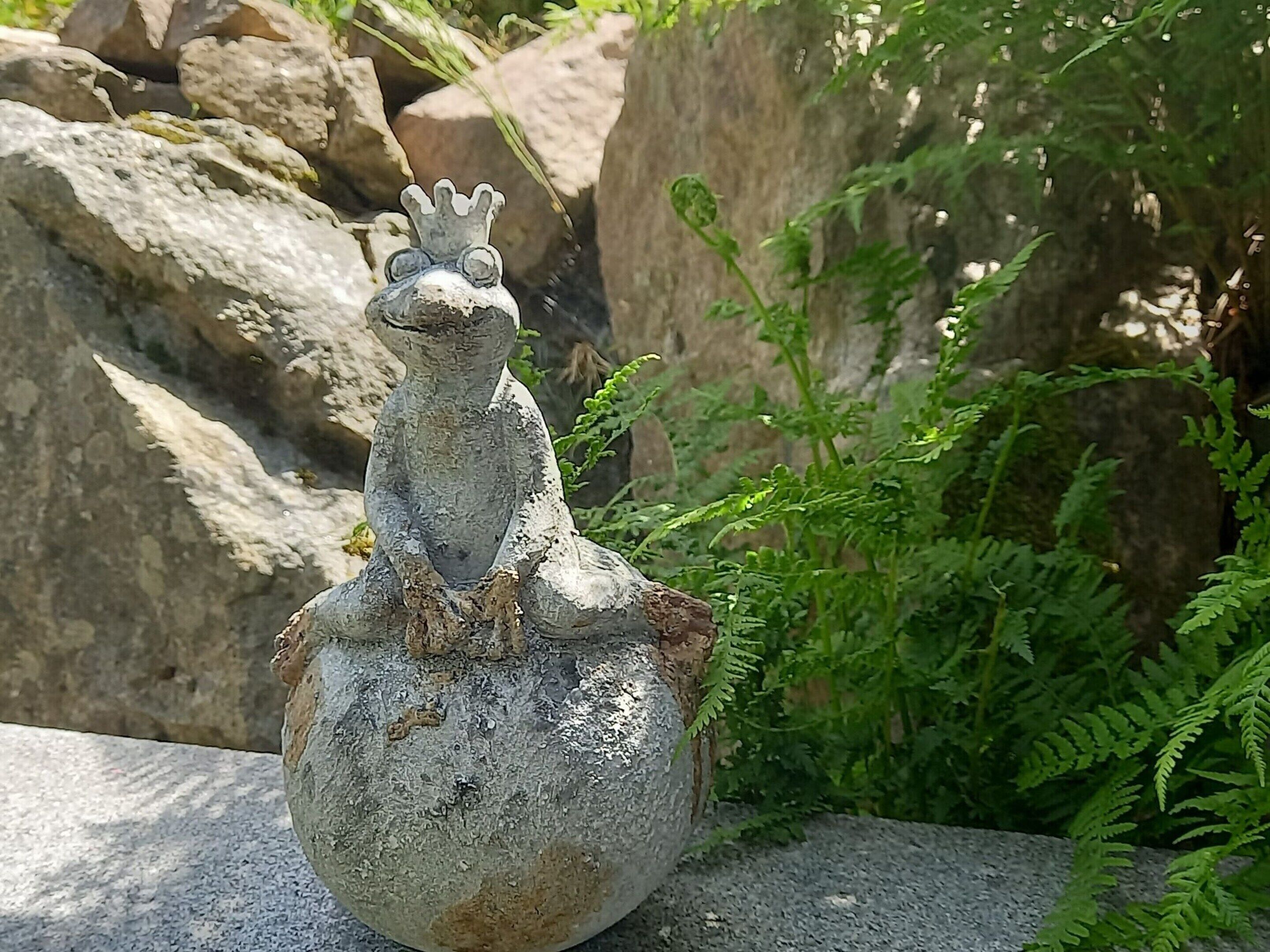 Une sculpture en forme de grenouille, surmontée d’une couronne, posée sur une surface en pierre.