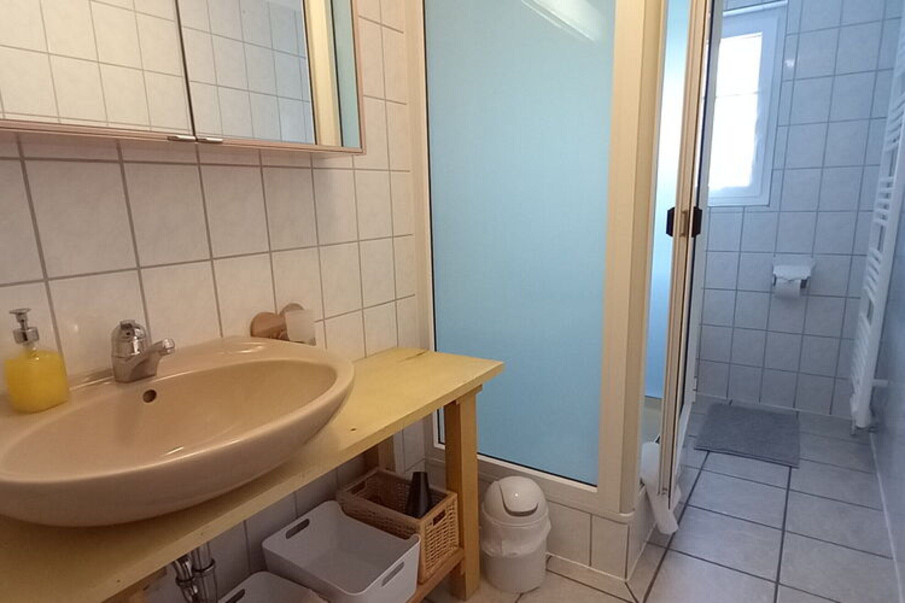 A bathroom with a beige sink, a mirror, and a shower area.