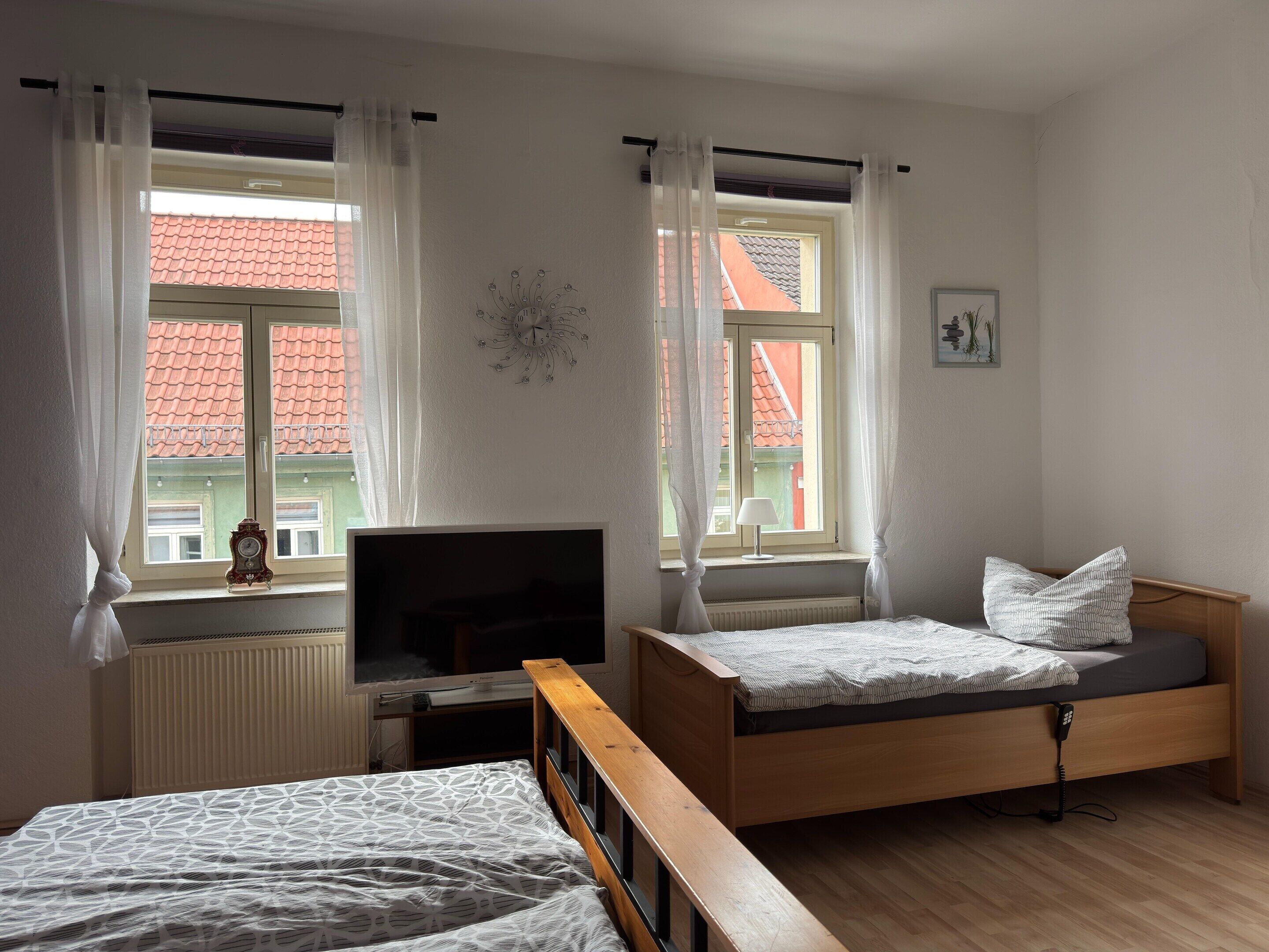 A bedroom with a bed, a TV, and two windows with curtains.