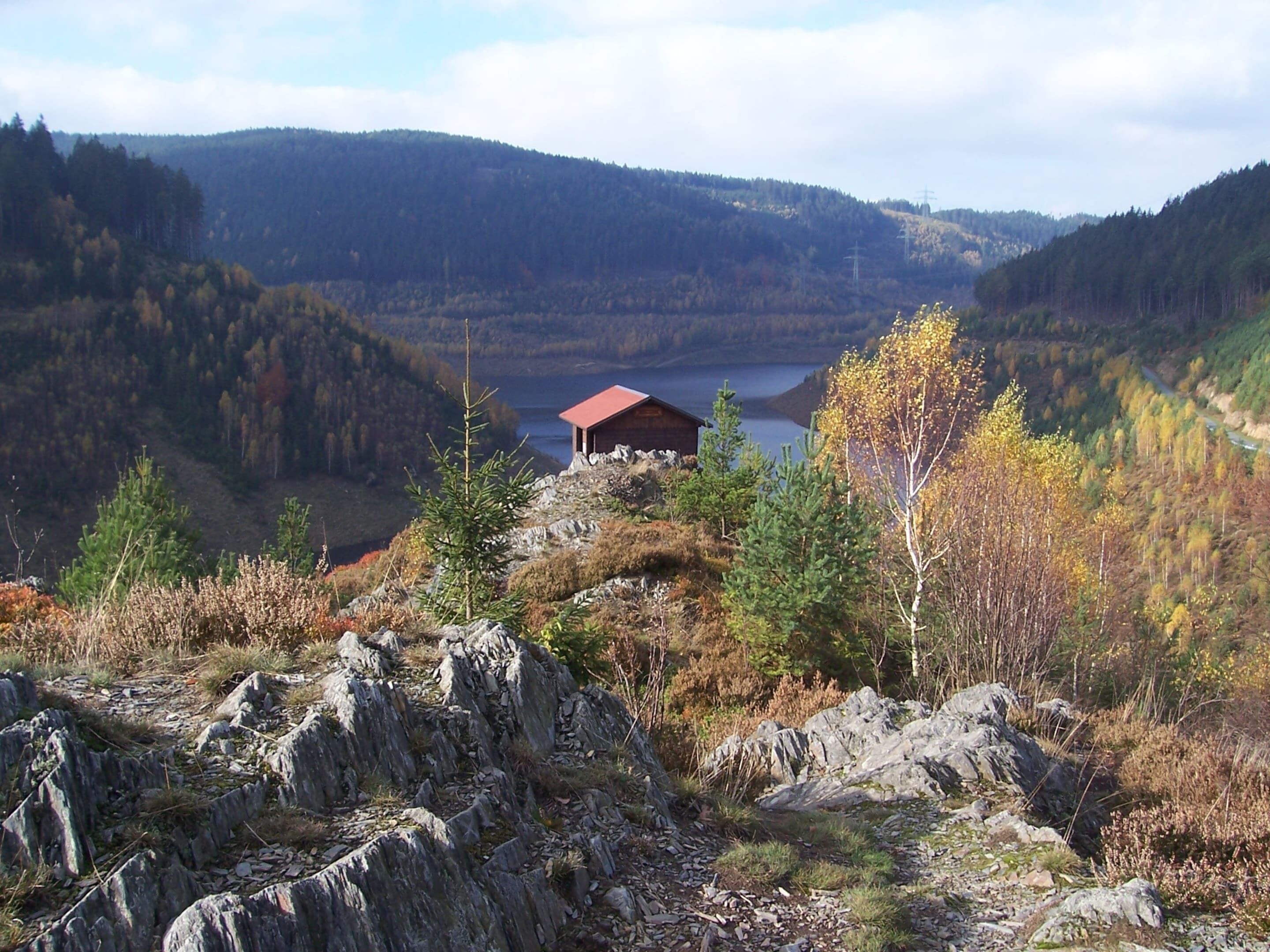 A cabin with a red roof surrounded by rocky terrain and autumn foliage.