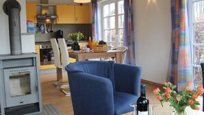 Un soggiorno accogliente con una poltrona blu, un tavolo da pranzo con un vaso di fiori e una cucina sullo sfondo.