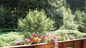 Una terraza de madera con una mesa y sillas, rodeada de flores coloridas y abundante vegetación.
