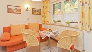 Una sala de estar acogedora con un sofá, dos sillas de mimbre, una mesa con un juego de té y una ventana con cortinas.
