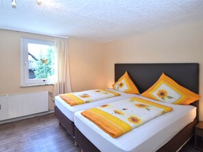 A double bed with a dark headboard, two single beds with matching headboards, a window with curtains, and a radiator.