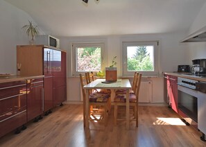 A kitchen with wooden cabinets, a dining table with chairs, a microwave, a stove, and a window with a view of trees.