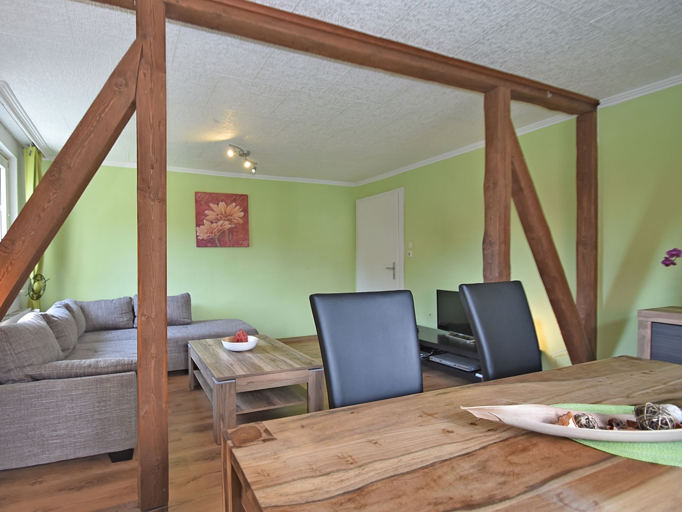 Una habitación con una mesa de madera para comer, dos sillas, un sofá y un televisor.