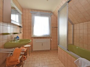 A bathroom with a green sink, a window with blinds, a white radiator, and a shower area.