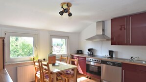 A kitchen with wooden flooring, a dining table with chairs, a stove, a dishwasher, and cabinets.
