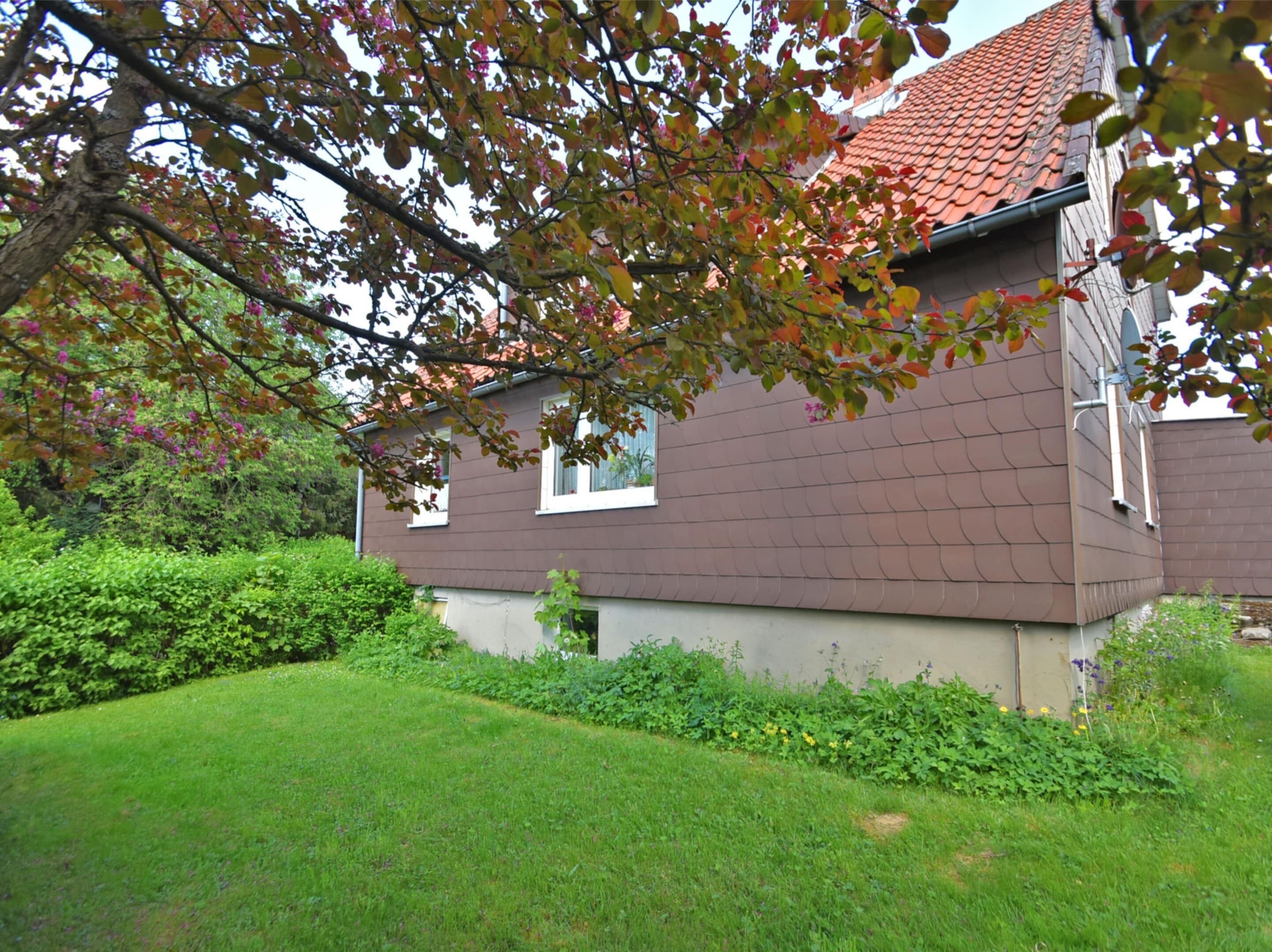 A house with a brown roof and beige walls, surrounded by a well-maintained lawn and greenery.