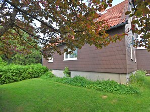 A house with a brown roof and beige walls, surrounded by a well-maintained lawn and greenery.