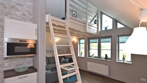 A loft-style bedroom with a wooden ladder, a built-in TV, and a view of the outdoors through large windows. - Ferienhaus in Obernburg am Edersee (Voehl)