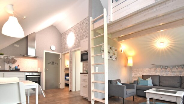 A modern apartment with a kitchen, dining area, and living room. It features a loft bedroom with a staircase, a wooden floor, and a blue rug. - Ferienhaus in Obernburg am Edersee (Voehl)