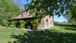 A stone house with a tiled roof, surrounded by a well-maintained lawn and trees. - Belvilla by Oyo Glicine in Italy (Modigliana)