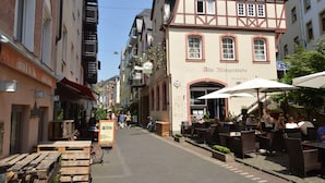 Una calle con mesas al aire libre, un edificio con la señalización 'Alte Winzerstube' y un cielo despejado.