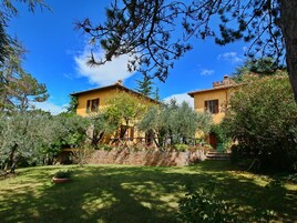 A two-story yellow building with a brick wall and a wooden fence in a garden.