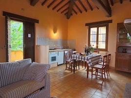 A cozy kitchen with a dining area, featuring a checkered tablecloth, wooden chairs, and a striped sofa.