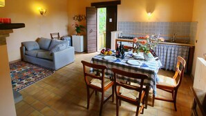 A cozy living room with a sofa, a dining table set for two, and a kitchen area with a sink and countertop. - Farmhouse in Todi With Pool & Theater Nearby (Todi)