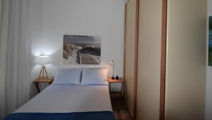 Une chambre d’hôtel avec un lit, une table de chevet, une lampe et un tableau représentant une plage accroché au mur.