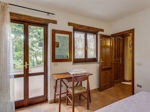 A room with a bed, a wooden chair, a small table, and a window with a view of trees. - Holiday Home in Assisi Near Monte Subasio (Assisi)
