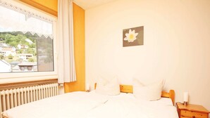 A bedroom with a large bed, wooden headboard, and a window with a view of houses. - Holiday Home Fabryshof in Bollendorf (Bollendorf)