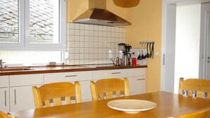 A kitchen with a wooden table, chairs, a stove, and a window with a view of a garden. - Stay With Garden in the Hunsruck (Stipshausen)