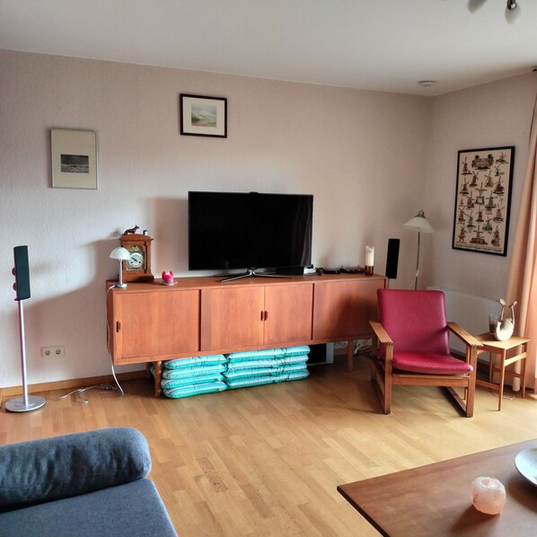 Ein Wohnzimmer mit Fernseher, einem roten Sessel, einer Couch und einem Holzschrank.