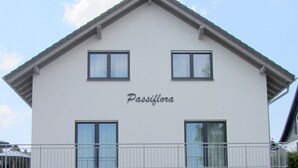 Un edificio de dos pisos llamado Passiflora, con balcón, garaje y un área de estar con sillas.