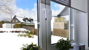 Una ventana con vista a un patio nevado, una caja de madera y dos plantas en macetas sobre el alféizar.