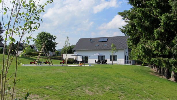 Una casa con techo inclinado, un patio con mobiliario exterior y un césped bien cuidado.