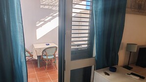 Une pièce dotée d’une porte coulissante, d’une petite table avec une chaise, d’un bureau avec une lampe et d’une fenêtre avec des stores.