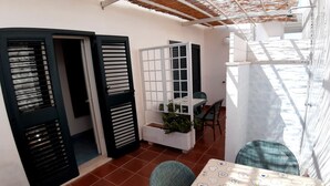 Un petit espace patio clos, avec une table et des chaises, un paravent blanc et une petite plante posée sur une étagère.