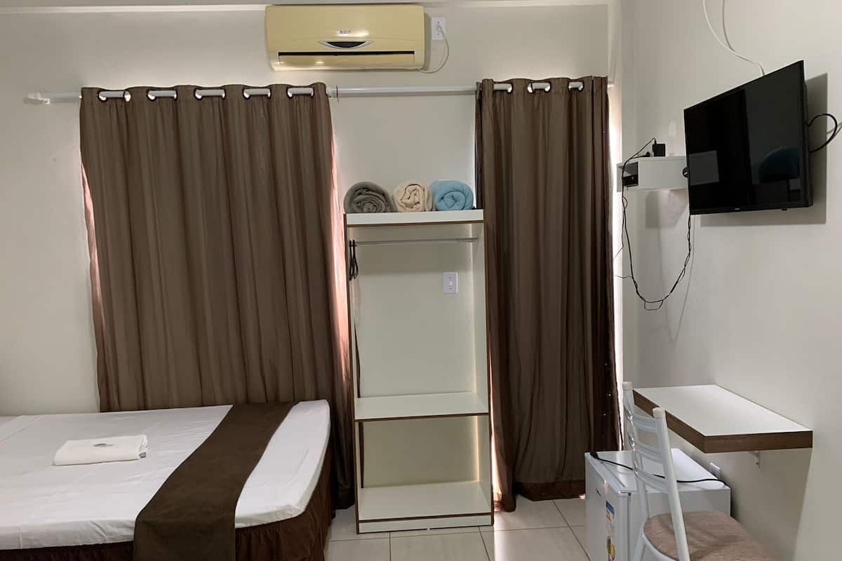 Una habitación de hotel con cama, escritorio, televisor, aire acondicionado y armario.