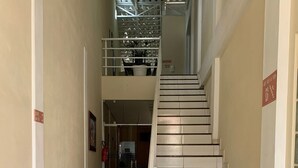 Una escalera conduce a un segundo piso, con barandilla de metal, piso de baldosas y extintor en la pared.